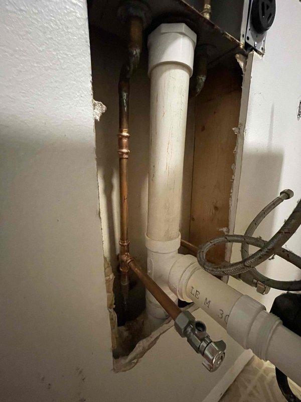 Completed re-route of laundry room water supply lines and drain system as previously sold. Accessed plumbing infrastructure through wall openings to reconfigure existing copper and PVC piping. Installed new shut-off valves with cross-handle operation and integrated water filtration system at supply connections. Rerouted vertical and horizontal drain lines using white PVC pipe with proper fittings and connections. Connected flexible supply lines to new valve configuration and verified all connections for proper water flow and drainage function.