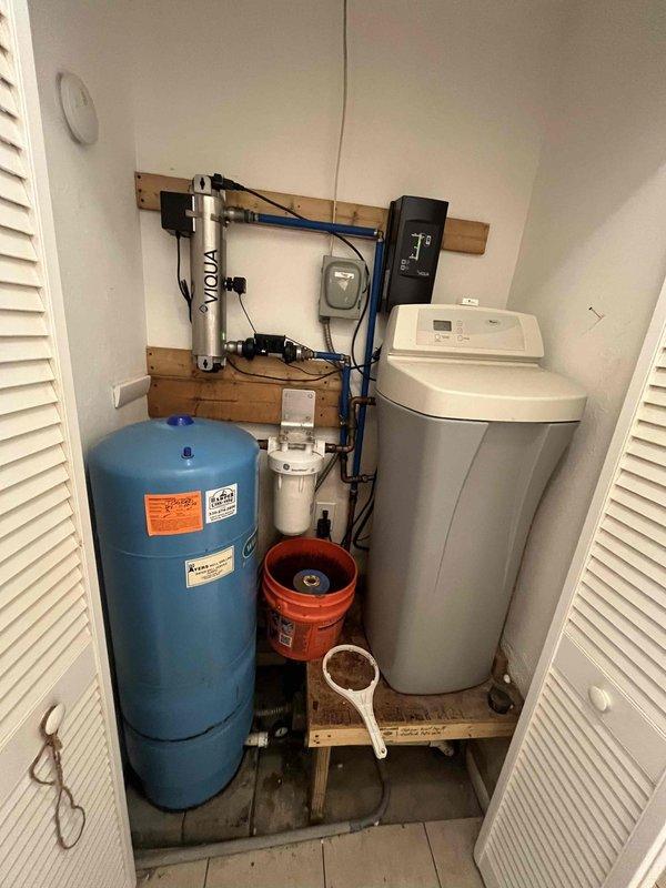 Responded to low water pressure complaint affecting entire residence that began approximately one week prior. Performed comprehensive diagnostic testing of well water system including pressure tank, filtration system, and water softener unit. Pressure gauge indicated correct static pressure, but actual flow pressure was significantly reduced throughout the home. Conducted systematic troubleshooting of all components in the utility closet water treatment system. Inspected blue pressure tank for proper air charge and bladder function, examined sediment filter housings for blockages, and tested water softener regeneration cycle and resin bed condition. Verified all valve positions and checked for potential restrictions in supply lines and distribution piping. Resolved pressure issue and restored normal water flow to all fixtures.
