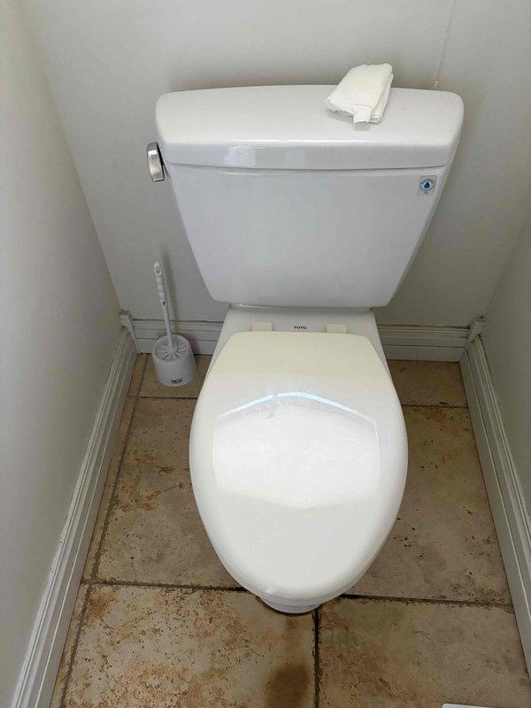 Responded to water leak complaint in basement below bathroom area. Upon inspection, examined bathroom fixtures and flooring for signs of water infiltration. Investigated toilet, flooring, and surrounding areas as potential leak sources. Documented conditions with photographs showing bathroom layout, toilet installation, and floor surfaces with visible staining patterns near toilet base and along baseboards, which may indicate chronic moisture issues or previous water events requiring further investigation of shower pan integrity and drain connections.