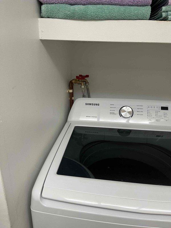 Completed follow-up repair service on Samsung top-loading washing machine water supply hoses. Inspected hose connections at wall-mounted shut-off valves with red handles, verified proper installation and secure fittings to prevent leaks, and confirmed washing machine is operating correctly with no water supply issues.