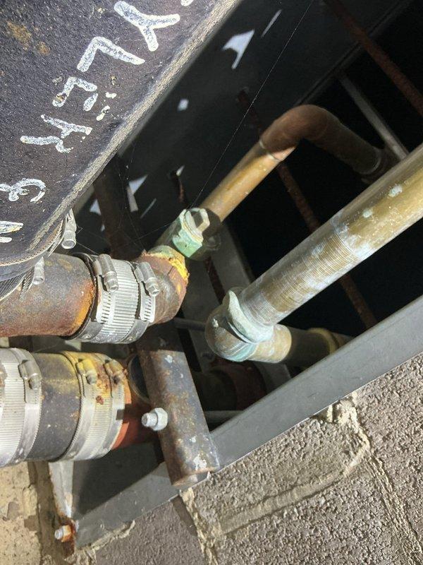 Conducted comprehensive plumbing assessment for correctional facility experiencing cross-contamination issues where flushing toilets in individual cells causes sewage backup into adjacent cells, affecting 18 total units. Inspected existing piping infrastructure which revealed severely corroded copper pipes with extensive oxidation, deteriorated flexible connectors secured with metal hose clamps, and compromised turquoise valve fittings throughout the system. Documented heavily rusted horizontal and vertical drainage lines, degraded pipe insulation with metal banding, and aging connection points that indicate systemic failure of the waste line configuration. Photographed critical areas including overhead access panels where corroded pipes enter service points and the complex arrangement of intersecting supply and waste lines. Prepared initial repipe estimate for single cell to establish scope and methodology for potential facility-wide remediation of the cross-connected plumbing system.
