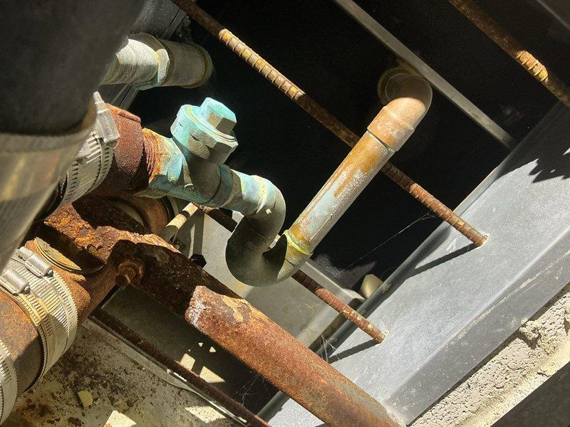 Conducted comprehensive plumbing assessment for correctional facility experiencing cross-contamination issues where flushing toilets in individual cells causes sewage backup into adjacent cells, affecting 18 total units. Inspected existing piping infrastructure which revealed severely corroded copper pipes with extensive oxidation, deteriorated flexible connectors secured with metal hose clamps, and compromised turquoise valve fittings throughout the system. Documented heavily rusted horizontal and vertical drainage lines, degraded pipe insulation with metal banding, and aging connection points that indicate systemic failure of the waste line configuration. Photographed critical areas including overhead access panels where corroded pipes enter service points and the complex arrangement of intersecting supply and waste lines. Prepared initial repipe estimate for single cell to establish scope and methodology for potential facility-wide remediation of the cross-connected plumbing system.
