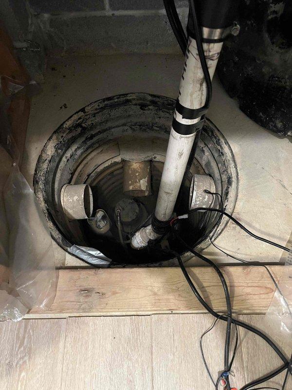 Responded to service call for 75-gallon gas power-vented water heater experiencing active leak from bottom of tank. Upon arrival, assessed unit and confirmed tank failure at base, indicating internal corrosion and breach of tank integrity. Instructed customer to shut off cold water supply valve to unit and open hot water taps throughout home to relieve system pressure and minimize further water damage. Documented existing conditions with photographs showing exterior utility connections and basement sump pump system managing water accumulation from failed water heater.
