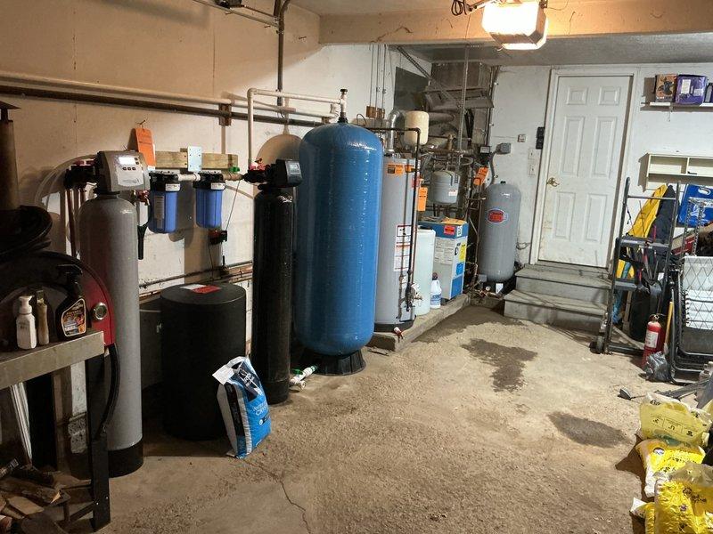 Completed installation of chlorine injection system and new sediment filter in basement mechanical room as return visit for previously sold equipment. System includes blue filtration canisters mounted to wall with copper and PVC distribution piping, pressure tank, and integrated controls with pressure gauge and shutoff valves. All components properly plumbed, tested for proper operation, and verified for adequate water pressure and chlorine dosing rates.
