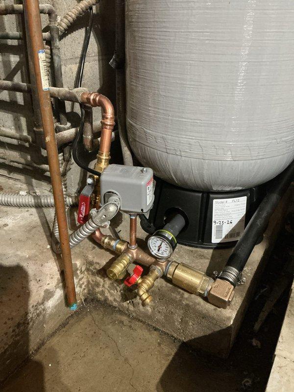 Completed installation of chlorine injection system and new sediment filter in basement mechanical room as return visit for previously sold equipment. System includes blue filtration canisters mounted to wall with copper and PVC distribution piping, pressure tank, and integrated controls with pressure gauge and shutoff valves. All components properly plumbed, tested for proper operation, and verified for adequate water pressure and chlorine dosing rates.