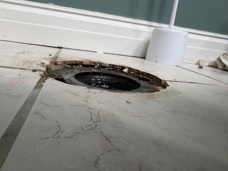 Returned to property to complete toilet rebuild in corner bathroom. Previous service had sold and initiated repair work that required follow-up completion. 

Upon arrival, assessed existing conditions including severely deteriorated floor structure surrounding toilet flange area. Large circular opening in subfloor exposed crawlspace below with extensive concrete deterioration, radiating cracks, and compromised wood framing. Evidence of long-term water damage and structural decay necessitated addressing underlying floor integrity before proceeding with toilet reinstallation.

Removed existing toilet to access damaged area. Inspected toilet tank components and identified deteriorated flapper valve, corroded hardware, and sediment accumulation requiring replacement. Rebuilt toilet mechanism with new fill valve assembly, flapper seal, flush components, and supply line connections. Cleaned tank interior and removed debris.

Addressed subfloor damage by removing compromised concrete and wood
