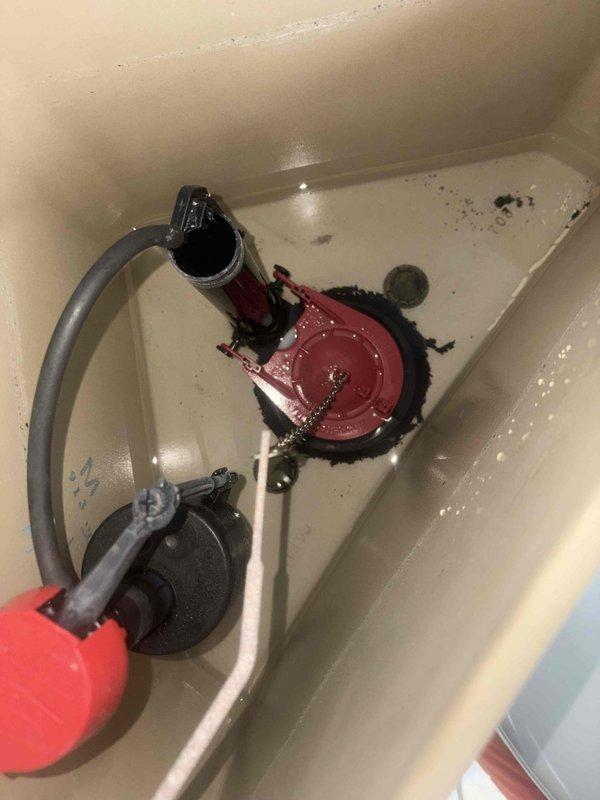 Returned to property to complete toilet rebuild in corner bathroom. Previous service had sold and initiated repair work that required follow-up completion. 

Upon arrival, assessed existing conditions including severely deteriorated floor structure surrounding toilet flange area. Large circular opening in subfloor exposed crawlspace below with extensive concrete deterioration, radiating cracks, and compromised wood framing. Evidence of long-term water damage and structural decay necessitated addressing underlying floor integrity before proceeding with toilet reinstallation.

Removed existing toilet to access damaged area. Inspected toilet tank components and identified deteriorated flapper valve, corroded hardware, and sediment accumulation requiring replacement. Rebuilt toilet mechanism with new fill valve assembly, flapper seal, flush components, and supply line connections. Cleaned tank interior and removed debris.

Addressed subfloor damage by removing compromised concrete and wood