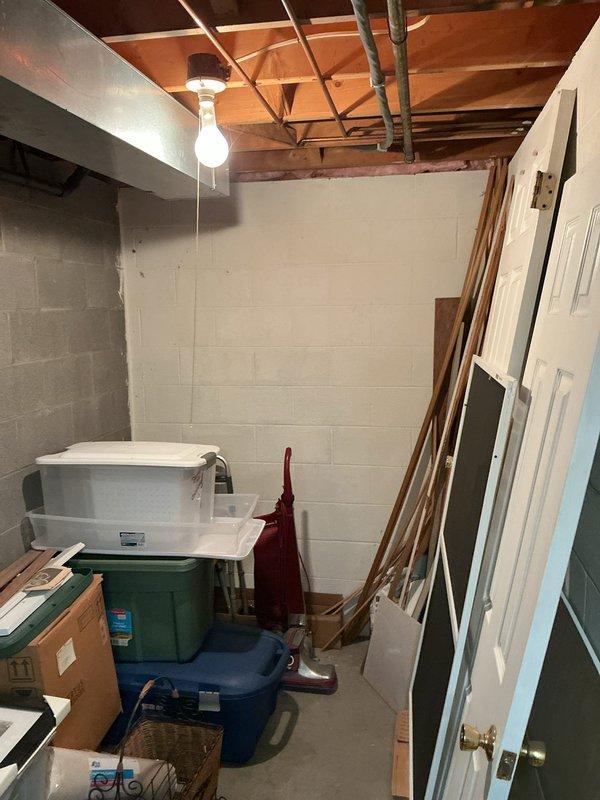 Performed site assessment for up-flush toilet installation in unfinished basement storage area. Evaluated existing plumbing infrastructure, structural layout, and available space among storage items and exposed ceiling joists. Documented conditions including concrete block walls, wooden beam ceiling structure, and current utility configuration to determine optimal placement and installation requirements for the up-flush toilet system.