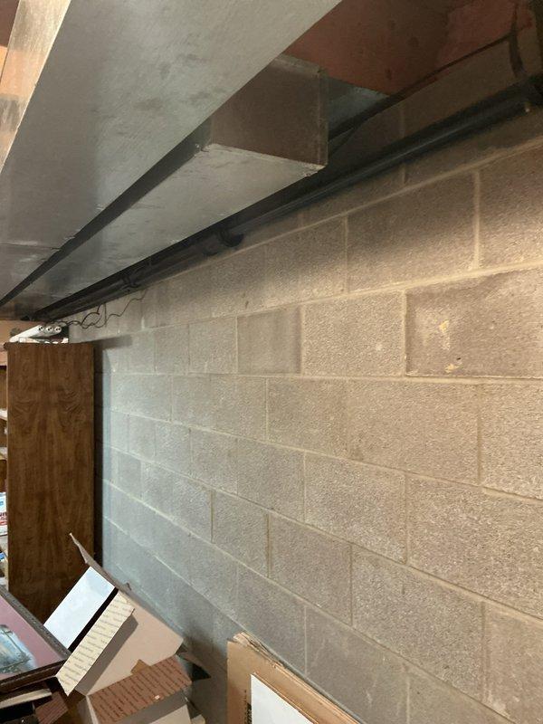 Performed site assessment for up-flush toilet installation in unfinished basement storage area. Evaluated existing plumbing infrastructure, structural layout, and available space among storage items and exposed ceiling joists. Documented conditions including concrete block walls, wooden beam ceiling structure, and current utility configuration to determine optimal placement and installation requirements for the up-flush toilet system.