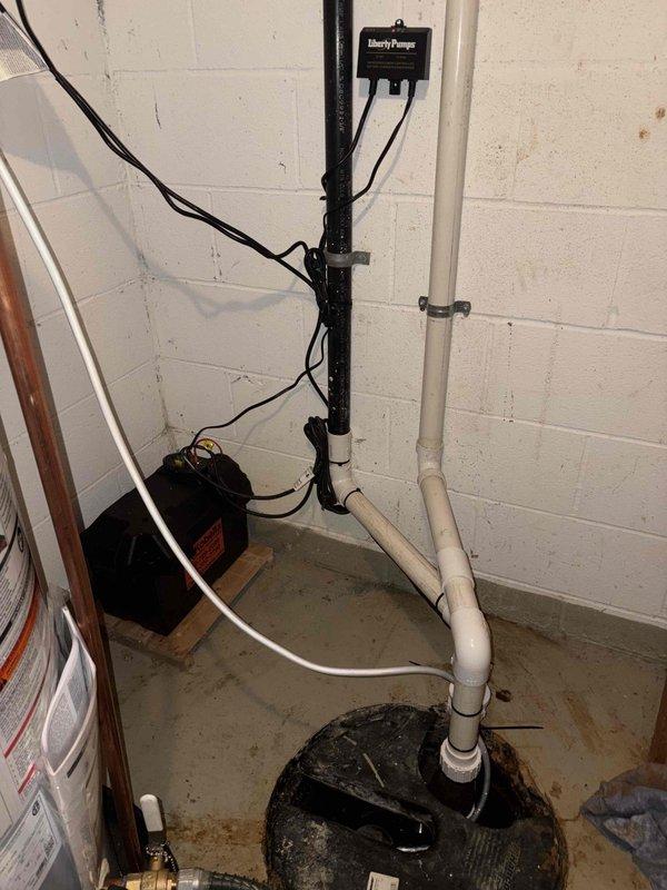Installed a 50-gallon gas power vented water heater with pump assembly and complete piping connections, including copper supply lines with shutoff valve and PVC venting system extending to ceiling joists. Installed Liberty Pumps sump pump system with battery backup in basement floor basin, featuring complete electrical connections, control box mounted to wall, white PVC discharge piping secured with metal clamps, and backup battery unit positioned on wooden block for flood protection.