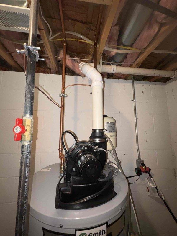 Installed a 50-gallon gas power vented water heater with pump assembly and complete piping connections, including copper supply lines with shutoff valve and PVC venting system extending to ceiling joists. Installed Liberty Pumps sump pump system with battery backup in basement floor basin, featuring complete electrical connections, control box mounted to wall, white PVC discharge piping secured with metal clamps, and backup battery unit positioned on wooden block for flood protection.