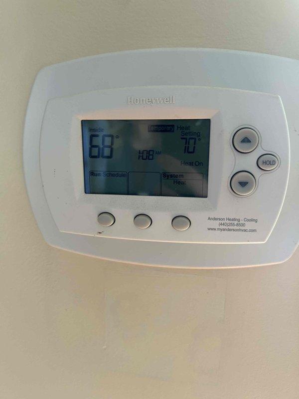 Responded to emergency no-heat call for fourteen-year-old furnace system. Upon arrival, verified thermostat was calling for heat with display showing 68°F inside temperature and 70°F setpoint with "Heat On" status indicated on Honeywell digital thermostat. Inspected furnace installation in basement mechanical room, including venting configuration and overall system condition. Documented equipment setup with water heater proximity and metal flue pipe routing. Performed diagnostic evaluation to identify cause of heating failure and restored heat to residence.