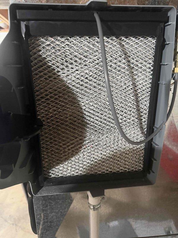 Performed scheduled preventive maintenance on the HVAC system and whole-house humidifier under the prepaid maintenance plan. Inspected the humidifier and found heavy mineral scale buildup on the evaporator pad, indicating the pad is due for cleaning or replacement. Verified electrical operation with a true-RMS clamp meter, measuring AC voltage at the unit to confirm proper supply.