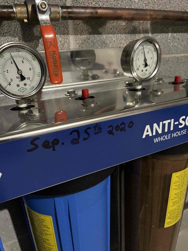 Inspected the installed whole-house anti-scale water filtration system, including the pressure gauges, manifold, inlet ball valve, pressure regulator, and the multi-stage filter housings, and found the unit intact with no visible leaks, cracks, or corrosion. Removed the spent, discolored filter cartridges from service and documented the equipment condition, noting the unit appears to date from a 2020 installation with no manufacturer identification beyond the valve labeling.