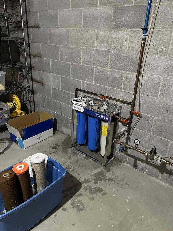 Inspected the installed whole-house anti-scale water filtration system, including the pressure gauges, manifold, inlet ball valve, pressure regulator, and the multi-stage filter housings, and found the unit intact with no visible leaks, cracks, or corrosion. Removed the spent, discolored filter cartridges from service and documented the equipment condition, noting the unit appears to date from a 2020 installation with no manufacturer identification beyond the valve labeling.