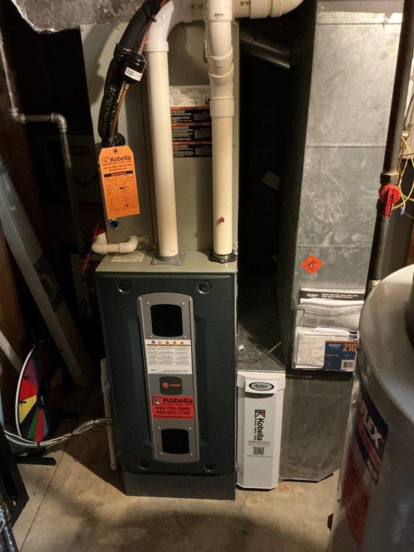 Performed a seasonal heating maintenance visit on a Trane gas furnace, replacing the pleated return air filter and labeling it with the service date for future reference. Inspected the furnace cabinet, wiring harness, PVC vent and condensate piping, and adjacent Aprilaire unit, finding no signs of frost, rust, or damage, and left the system operating normally with the service tag attached.