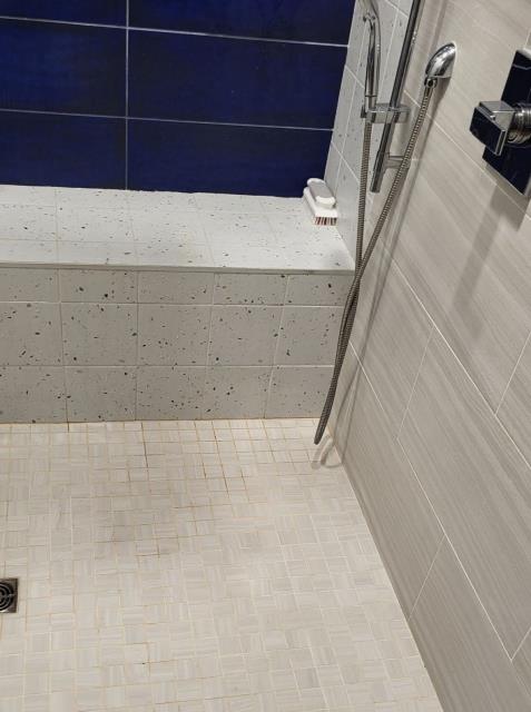 We responded to our customer due to a leak coming from the shower that was only occurring while the shower was in use. Upon arrival, we inspected the shower, we ran the shower and also inspected the basement, where we were able to confirm active leaking. Our customer also provided us a video showing the water appearing below the corner of the shower bench at the wall of the shower. The sheetrock had already been opened around the water lines and shower valve, and all plumbing connections in that area were found to be dry. After running the water for an extended period, we observed moisture surfacing where the shower meets the plastic edge strip. Based on our findings, the plumbing itself is not leaking. This appears to be a failure in the tile, grout or water proofing system that is allowing water to escape and travel into the basement. 