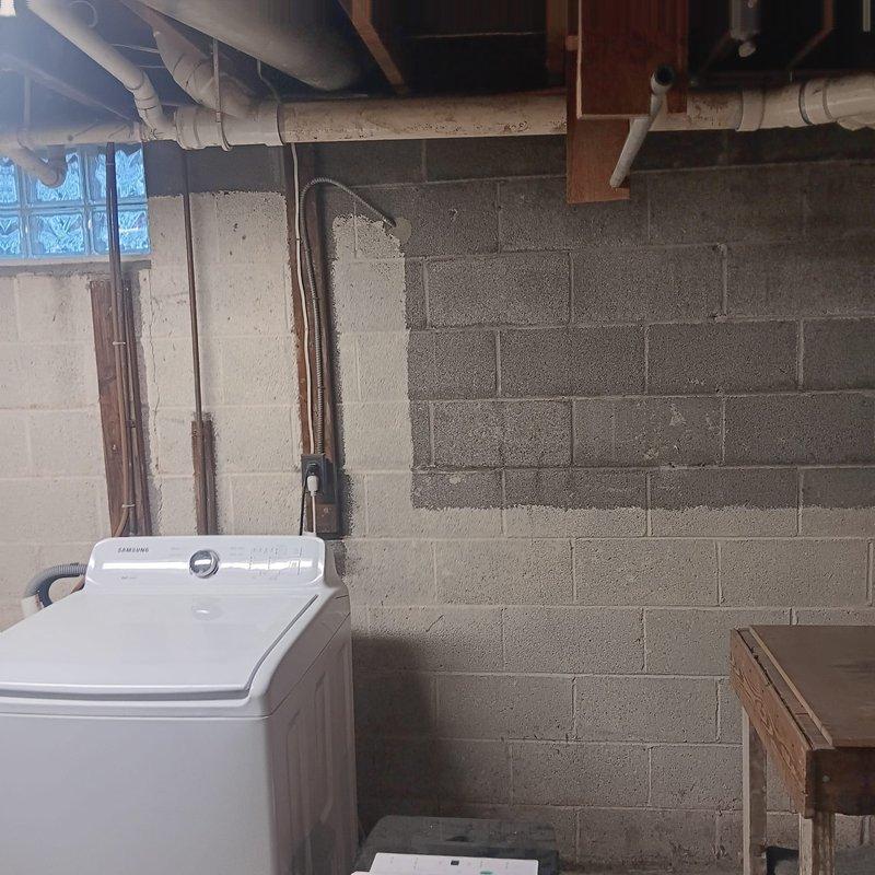 Completed estimate for replacement of existing wax ring and installation of a pump system to redirect laundry drain discharge to septic tank. Documented existing plumbing configuration in utility area, including washing machine location and current drainage setup. Installation will involve PVC piping connections to new green pump unit mounted on concrete floor with appropriate brackets and electrical connections.