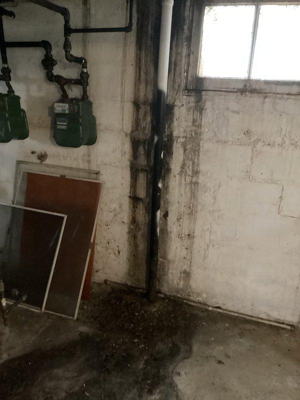 Responded to a water leak service call at a multi-unit property. Upon inspection, discovered significant water damage behind kitchen wall with previous wall opening in lower unit revealing a cracked drain pipe that was not the active leak source. Observed substantial water staining on basement concrete block walls and deterioration indicating prolonged moisture exposure. Determined the property requires comprehensive replumbing with replacement of the aging galvanized water lines, which are also causing low cold water pressure in the upper unit.