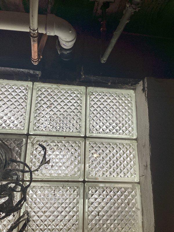 Responded to emergency water leak report in bathroom. Upon inspection, discovered significant water damage to wooden joists and structural elements in the crawlspace below, with visible deterioration and possible mold formation. Located source of leak at corroded copper pipe connection near glass block wall, replaced damaged section with new PVC fittings to restore proper function and prevent further structural damage.