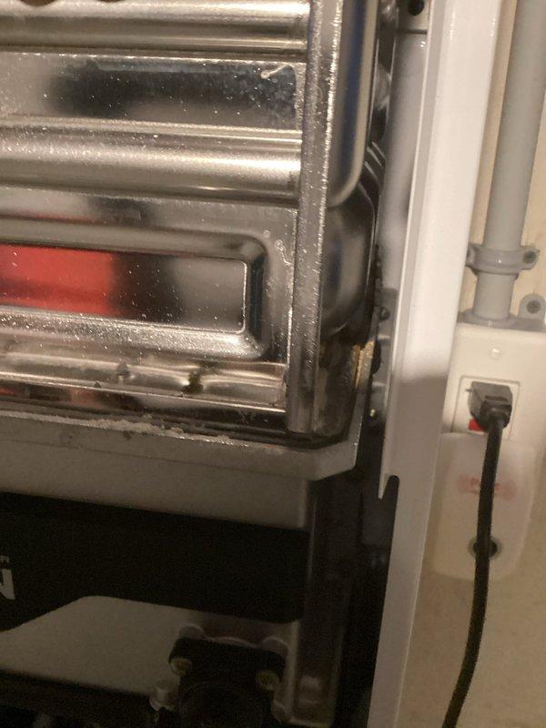 Performed follow-up inspection of Navien tankless water heater system. Took detailed photographs of external housing and internal components including pump assembly, drainage connections, and control interface to document current condition. Noted some mineral deposits on metal framing and dust accumulation around panel edges.