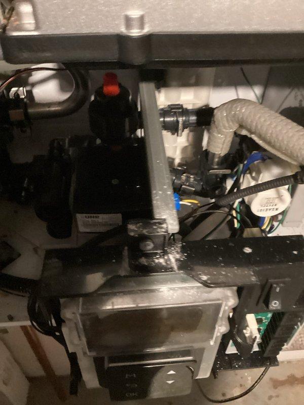 Performed follow-up inspection of Navien tankless water heater system. Took detailed photographs of external housing and internal components including pump assembly, drainage connections, and control interface to document current condition. Noted some mineral deposits on metal framing and dust accumulation around panel edges.