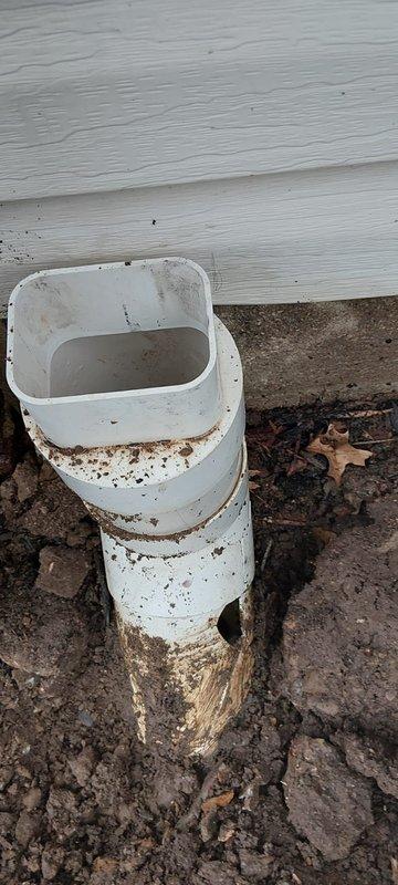 Responded to service call for a clogged and broken downspout line on a 30-year-old home. Upon inspection, found damaged connector at the base of the downspout where it meets the ground drainage system. Installed new PVC downspout drainage components, ensuring proper connection between the rectangular upper section and the round pipe below to restore proper water flow away from the foundation.
