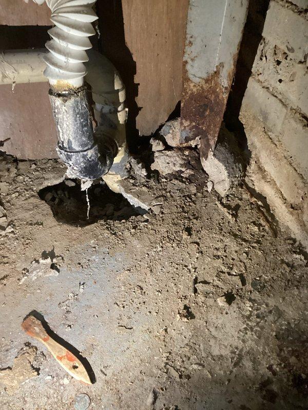 Upon inspection of basement laundry tub, identified severely corroded metal P-trap with active leakage causing significant water damage to surrounding wooden framing members and floor. Removed deteriorated metal trap assembly and installed new code-compliant PVC P-trap with proper connections to existing drain line, restoring proper drainage function and eliminating leak.