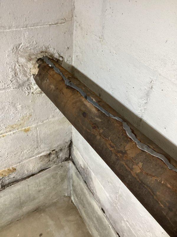 Inspected leaking cast iron waste pipe leading to septic system. Observed significant corrosion and improper sealing at wall penetration point with visible water damage. System contains a mix of older cast iron piping and newer PVC components with deterioration at connection points requiring attention.