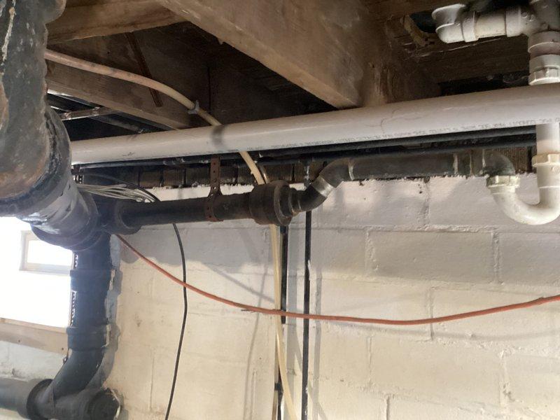 Inspected leaking cast iron waste pipe leading to septic system. Observed significant corrosion and improper sealing at wall penetration point with visible water damage. System contains a mix of older cast iron piping and newer PVC components with deterioration at connection points requiring attention.