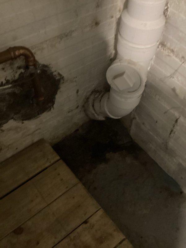 Diagnosed and repaired a leaking soil stack in basement utility area with significant water damage to surrounding walls and floor. Identified severe corrosion at copper pipe junction and deterioration of PVC drainage system components. Replaced damaged pipe sections, fittings, and clean-out access cap, then sealed all connections to prevent further leakage.