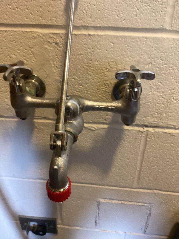 Responded to service call for clogged drain in men's restroom where preliminary work had been started by another technician. Completed drain clearing in the restroom and serviced a utility sink faucet with weathered cross-handle valves and red cap adapter. Additionally, addressed flush meter issues on urinal to restore proper functionality.