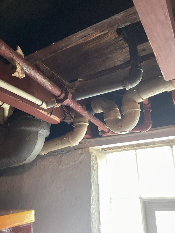 Conducted an estimate for shower valve and waterline replacement. Current installation shows aged copper pipes with visible corrosion beneath floor joists alongside newer PVC sections. Bathroom examination revealed damaged tile surrounding the shower head fixture and an outdated bathtub with mint green interior requiring comprehensive plumbing system updates.