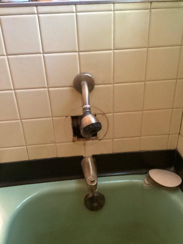 Conducted an estimate for shower valve and waterline replacement. Current installation shows aged copper pipes with visible corrosion beneath floor joists alongside newer PVC sections. Bathroom examination revealed damaged tile surrounding the shower head fixture and an outdated bathtub with mint green interior requiring comprehensive plumbing system updates.