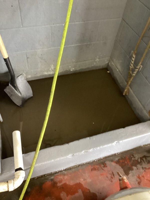 Responded to service call for clogged drain in flooded concrete basin. Upon arrival, found significant water accumulation in utility area with two drains submerged under muddy brown water. Successfully cleared blockage and restored proper drainage function to prevent future flooding.
