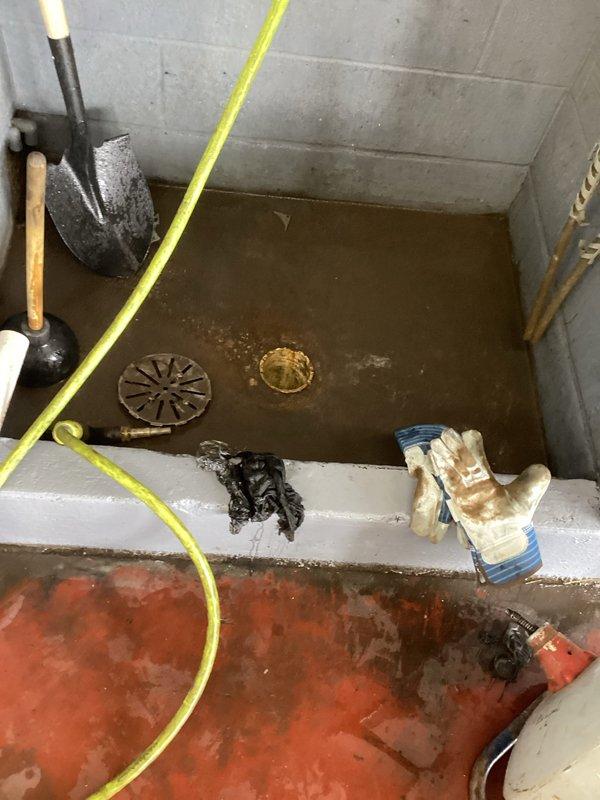 Responded to service call for clogged drain in flooded concrete basin. Upon arrival, found significant water accumulation in utility area with two drains submerged under muddy brown water. Successfully cleared blockage and restored proper drainage function to prevent future flooding.