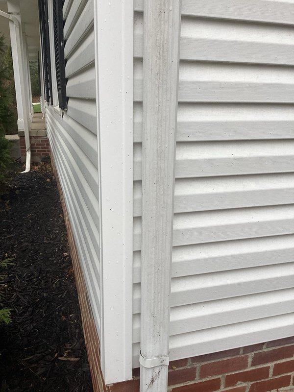 Conducted inspection of residential downspout system, identifying right downspout requiring full replacement. Observed existing white vinyl downspout with visible deterioration at corner junction and disconnection at base. Noted accumulation of debris and leaf matter around foundation area potentially causing improper drainage. Replacement recommended to prevent water damage to foundation and landscaping.