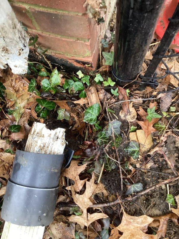 Conducted inspection of residential downspout system, identifying right downspout requiring full replacement. Observed existing white vinyl downspout with visible deterioration at corner junction and disconnection at base. Noted accumulation of debris and leaf matter around foundation area potentially causing improper drainage. Replacement recommended to prevent water damage to foundation and landscaping.