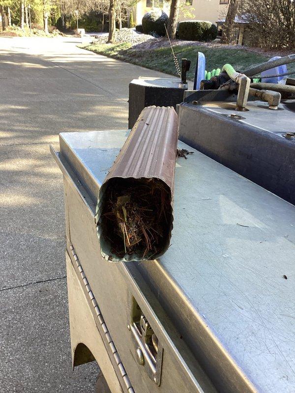 Responded to report of water backing up from downspout near front entrance. Upon inspection, located and accessed the underground downspout drainage line. Discovered significant blockage consisting of accumulated leaves, twigs, and organic debris completely obstructing the corrugated metal drain pipe. Removed the clogged section and cleared all debris from the line to restore proper water flow and drainage function.