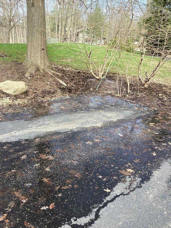 Responded to service call for water leak in residential flower bed area. Upon arrival, observed active water leakage around landscaped mulch bed near driveway. Conducted visual inspection of affected area, including examination of ground saturation patterns and surface conditions. Documented site conditions with photographs showing dormant plantings in circular mulch bed adjacent to concrete driveway and cracked asphalt surfaces. Assessment indicated potential underground pipe failure beneath landscaped area based on leak location and severity. Marked suspected leak zone with identification stake for future excavation reference.