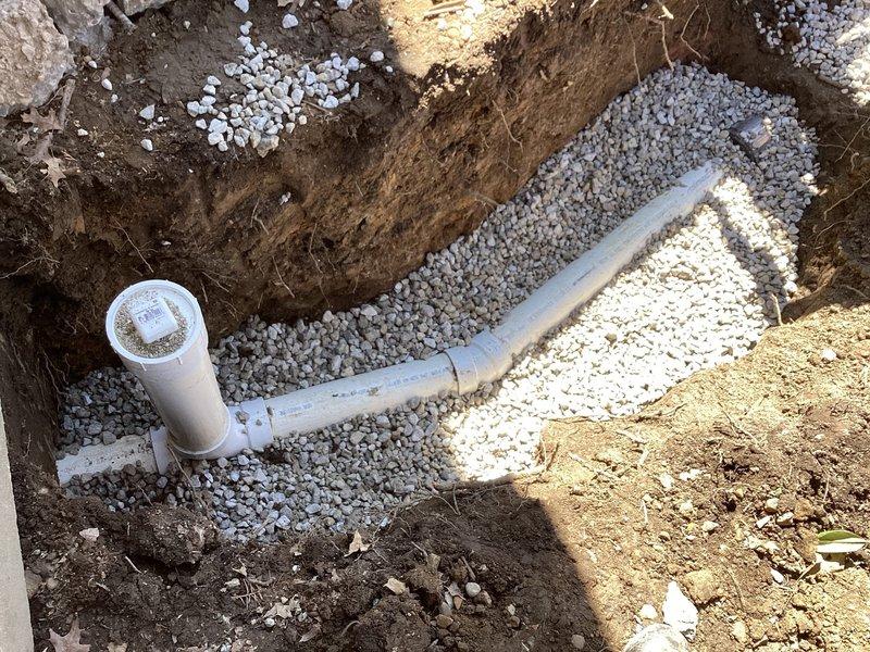 Excavated and exposed existing sewer line to locate and repair damaged section. Installed new white PVC piping with proper fittings and elbow joints, bedded in crushed stone aggregate within properly dimensioned trench. Verified integrity of remaining pipe system and backfilled excavation upon completion of repairs.