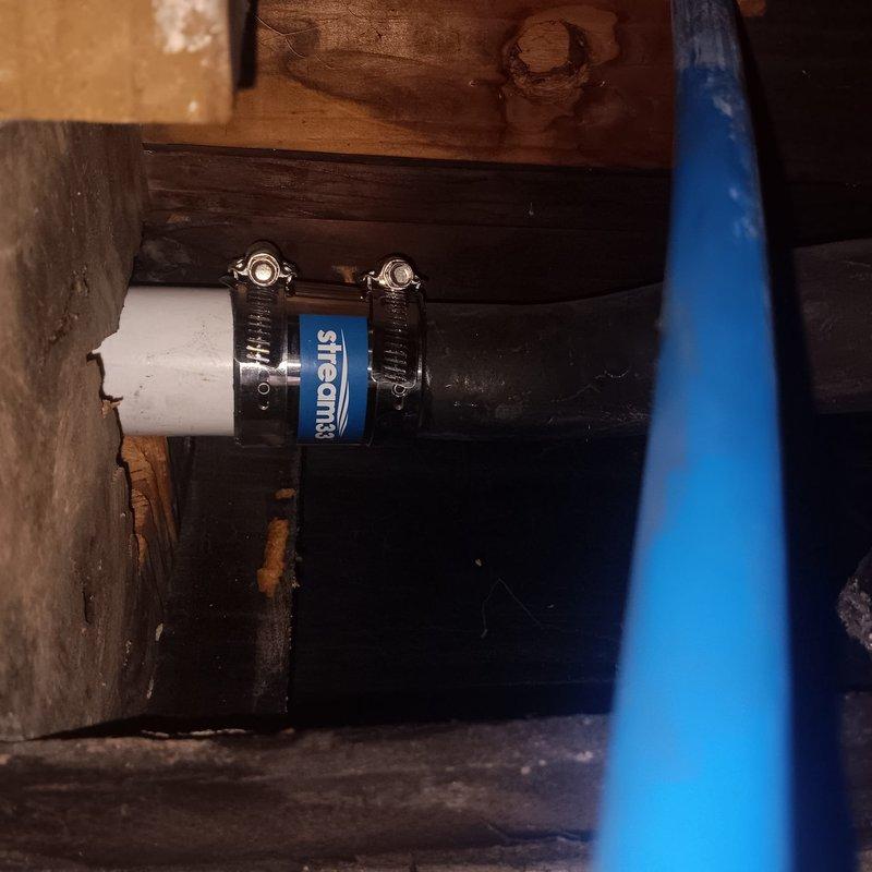 Responded to callback for active water leak from toilet penetrating through floor into kitchen ceiling below. Upon inspection, located source of leak at deteriorated toilet flange connection in second-floor bathroom. Discovered damaged wax ring seal and compromised drain pipe coupling beneath toilet, allowing wastewater to bypass plumbing system and seep through subfloor into kitchen area below. 

Accessed crawl space to assess extent of water damage and verify leak path. Found makeshift repair coupling connecting white PVC drain line to black ABS pipe with metal hose clamps, which had failed and was actively leaking. Removed temporary coupling and installed proper ABS to PVC transition coupling with approved primer and cement per code requirements. Reset toilet with new wax ring seal and closet bolts, ensuring proper flange engagement and watertight connection.

Documented deteriorated ductwork insulation in attic space near plumbing penetration, noting severe degradation of vapor bar