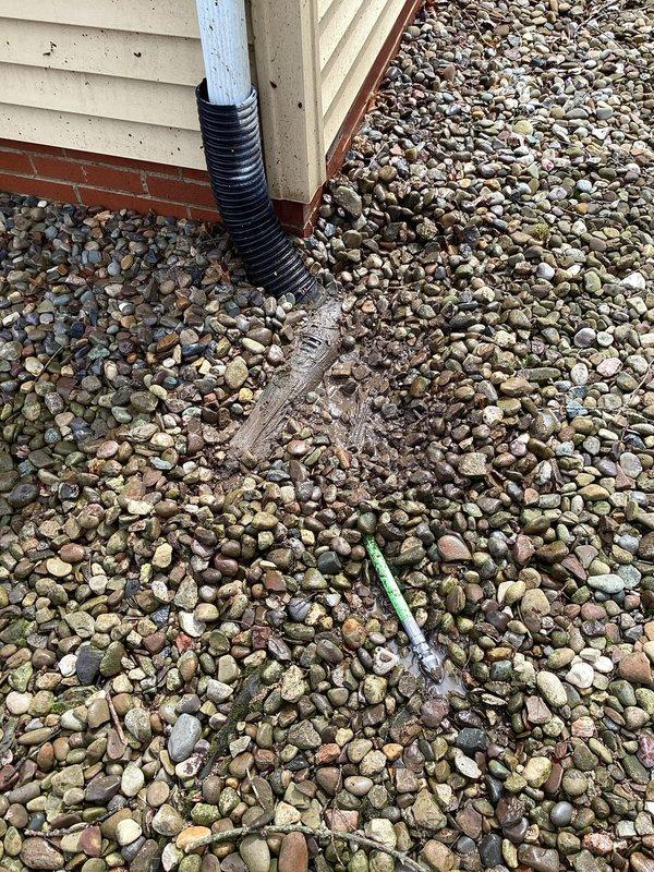 Responded to report of gutter drain lines overflowing at Unit A, causing water to redirect toward exterior walls and foundation. Upon arrival, located the main drain cleanout at building exterior where downspout connects to underground drainage system. Accessed drainage grate set in river rock bed at foundation level. Snaked the clogged drain line to remove blockage and restore proper water flow through the gutter drainage system, preventing water accumulation near building foundation and exterior walls.