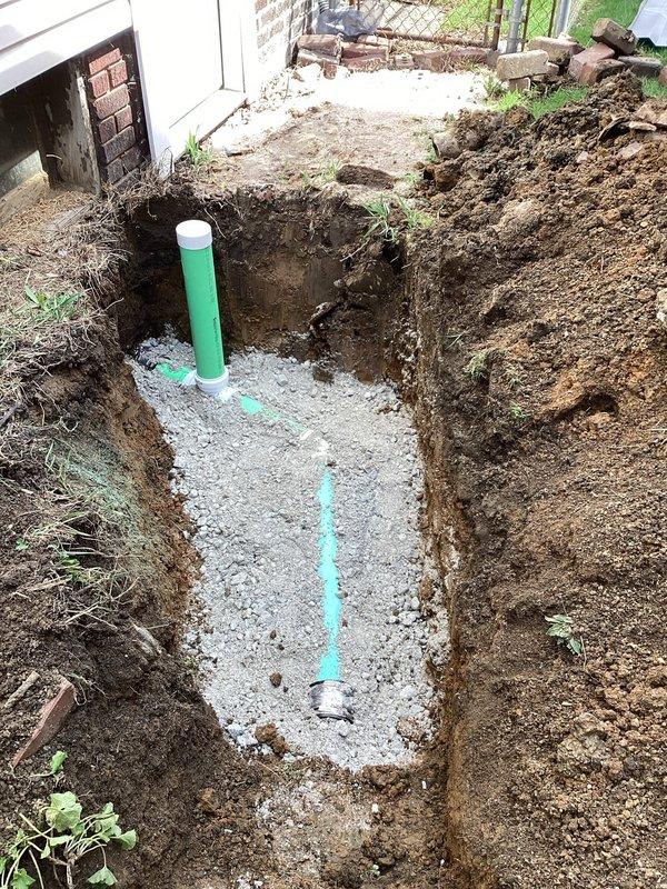 Excavated trench along right side of residential structure to access and replace damaged sewer lateral line. Removed approximately 10 feet of deteriorated piping and installed new PVC sewer pipe with proper fittings and connections. Laid pipe on crushed stone bedding material for adequate support and drainage. Installed exterior cleanout access point with green riser pipe and white cap for future maintenance accessibility. Performed camera inspection of remaining sewer line to verify system integrity and identify any additional issues downstream. Backfilled excavation upon completion of repairs.