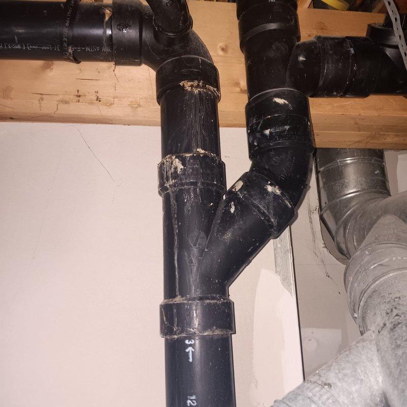 Responded to a reported small leak on the basement drain pipe connected to the main plumbing stack in a 25-year-old residential property. Upon arrival, conducted a thorough inspection of the drainage system and identified deterioration on the black ABS piping, with visible surface wear, peeling coating, and compromised pipe integrity at multiple connection points. The aging pipe material showed significant degradation consistent with the home's age, with white residue and flaking sections indicating long-term moisture exposure and material breakdown.

Assessed the complete plumbing configuration, including the junction points, elbow connections, and vertical sections of the main stack assembly. Documented the condition of all affected piping, noting the metal clamp fasteners and connection points where leakage was occurring. Evaluated the surrounding copper supply lines and confirmed they were properly secured to the floor joists with appropriate fasteners.

Performed necessary repairs