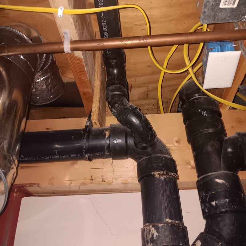 Responded to a reported small leak on the basement drain pipe connected to the main plumbing stack in a 25-year-old residential property. Upon arrival, conducted a thorough inspection of the drainage system and identified deterioration on the black ABS piping, with visible surface wear, peeling coating, and compromised pipe integrity at multiple connection points. The aging pipe material showed significant degradation consistent with the home's age, with white residue and flaking sections indicating long-term moisture exposure and material breakdown.

Assessed the complete plumbing configuration, including the junction points, elbow connections, and vertical sections of the main stack assembly. Documented the condition of all affected piping, noting the metal clamp fasteners and connection points where leakage was occurring. Evaluated the surrounding copper supply lines and confirmed they were properly secured to the floor joists with appropriate fasteners.

Performed necessary repairs