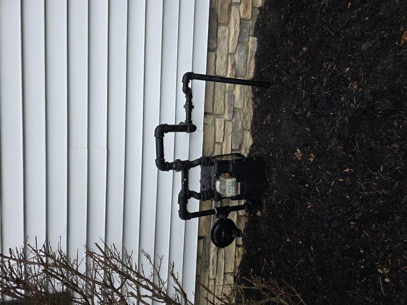 Completed installation of approximately 20 feet of underground gas piping with 1-inch risers to exterior building wall. Installed black iron pipe assembly with multiple fittings, pressure regulator, and meter connection point, mounting entire configuration at the junction between white siding and stone veneer exterior. All connections were properly fitted, tested, and secured according to code requirements for residential gas service.