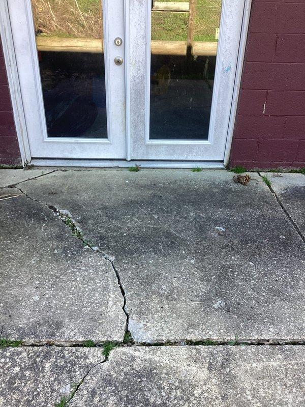 Responded to flooding issue affecting basement and garage areas. Upon inspection, observed water infiltration problems with existing trench drain system proving inadequate for current groundwater volume. Assessed interior basement utility area showing evidence of water accumulation on concrete floor surfaces. Evaluated exterior entrance area where significant foundation settlement and concrete paver cracking was creating direct water pathways toward building. Documented compromised drainage conditions including structural cracks in walkway allowing surface water penetration. Recommended enhanced drainage solutions to address insufficient capacity of current system and prevent continued water intrusion into below-grade spaces.