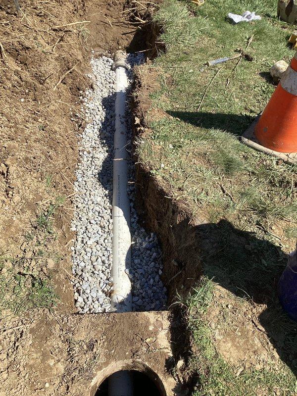 Excavated and exposed existing sewer line to access defective outlet tee fitting at lower grade elevation. Removed failed tee connection and installed new outlet tee assembly with proper blue PVC fittings to restore functionality. Backfilled trench with drainage gravel in stages, utilizing white crushed stone and darker aggregate material for proper compaction and drainage support around the repaired pipe section.