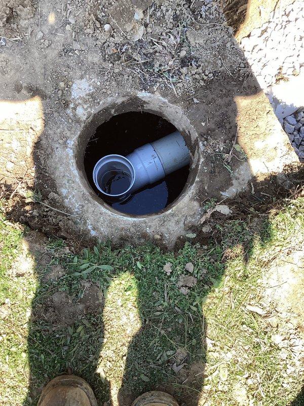 Excavated and exposed existing sewer line to access defective outlet tee fitting at lower grade elevation. Removed failed tee connection and installed new outlet tee assembly with proper blue PVC fittings to restore functionality. Backfilled trench with drainage gravel in stages, utilizing white crushed stone and darker aggregate material for proper compaction and drainage support around the repaired pipe section.